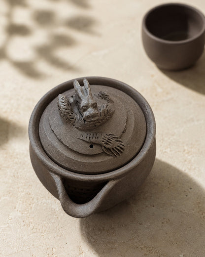 Hōhin lit by leaf shadows, dark teacup behind, strainer holes visible in the mouth.