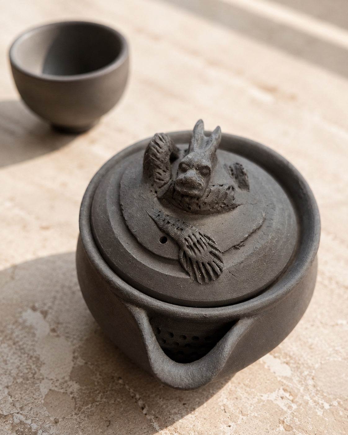 Hōhin and dark teacup on stone, dragon finial and pierced strainer both visible.
