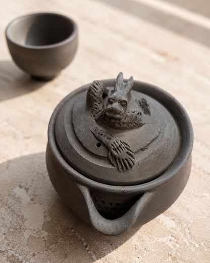 Hōhin and dark teacup on stone, dragon finial and pierced strainer both visible.