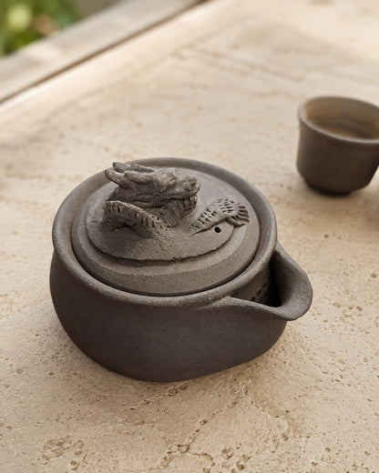 Charcoal unglazed stoneware hōhin teapot with hand-modelled dragon finial, three-quarter view.